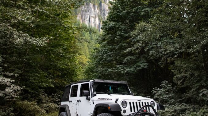 4x4 offroad Une Jeep Wrangler robuste sur une route de gravier entourée d'une forêt luxuriante et de montagnes imposantes.